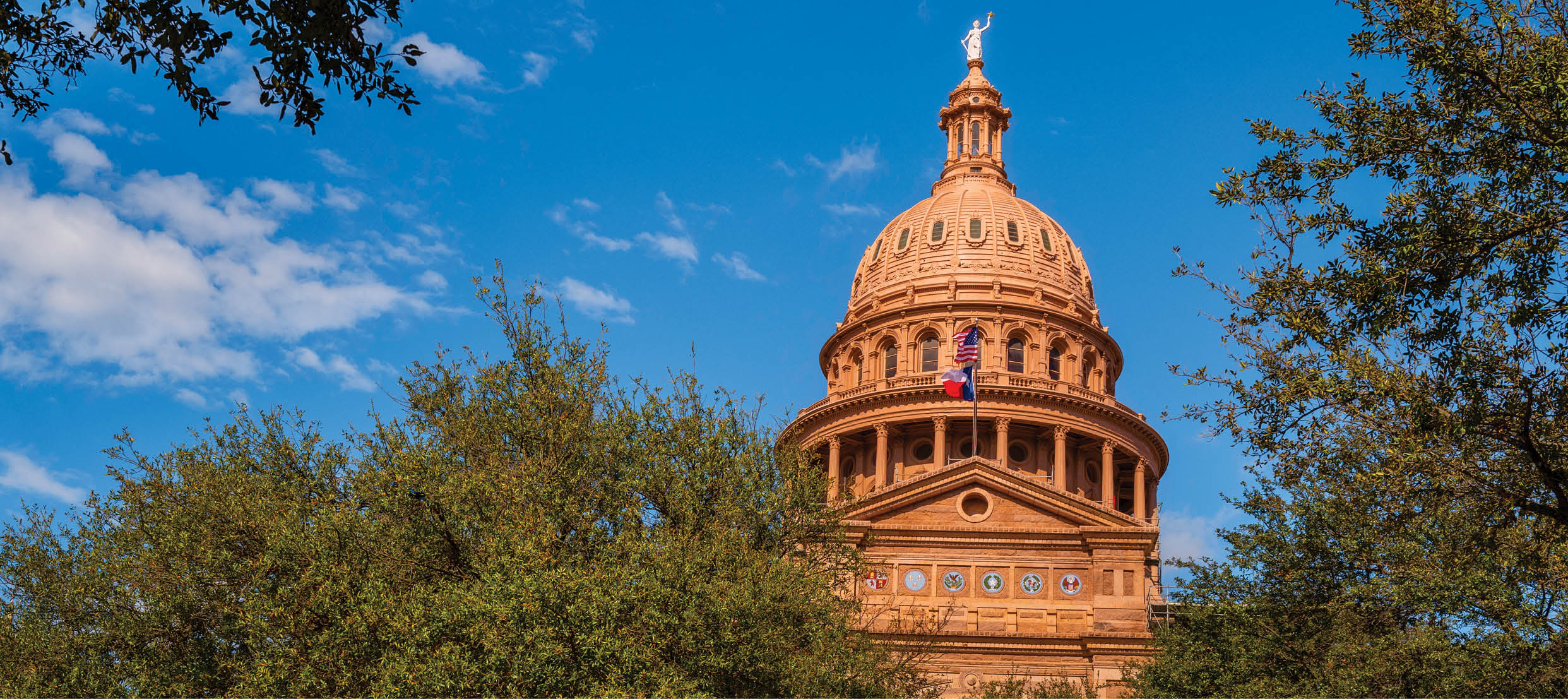 Texas State Capitol Building in Austin, the tallest state capitol in the United States, with the sunset red granite rooftop illuminated by the sunrays over the live oak trees