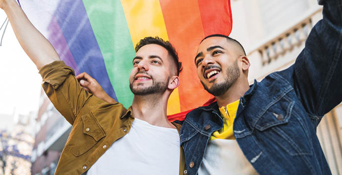 Portrait of young gay couple embracing and showing their love with rainbow flag at the street. LGBT and love concept.