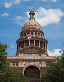 Dome of the State Capitol building, Austin, Texas, USA against a blue sky and clouds, trees in foreground