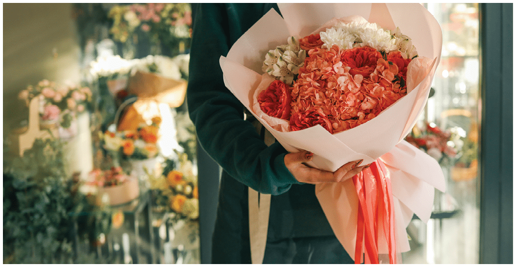 Elegant bouquet with hydrangeas, roses, and delicate flowers wrapped in soft pastel paper with bright ribbons, held by a florist in a cozy flower shop, highlighting vibrant blooms.