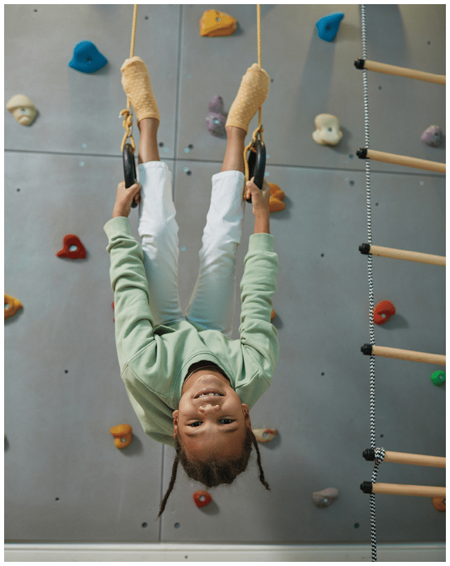 Full length portrait of active black child hanging upside down on sports rings at home and having fun