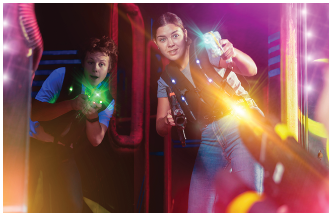 Two exciting players guy and woman with laser weapons in dark laser tag room