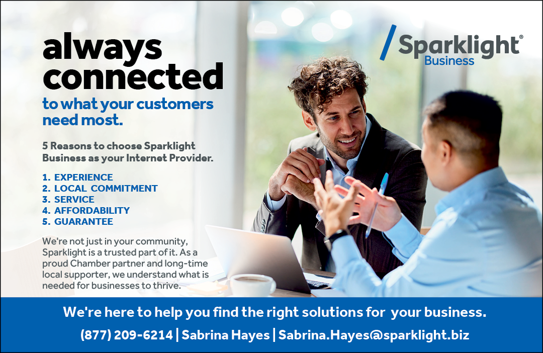 Two men are talking to each other in front of a laptop. They are both wearing suits and ties. The laptop is open and has a coffee cup on it. The men are discussing Sparklight business solutions. AI generated content