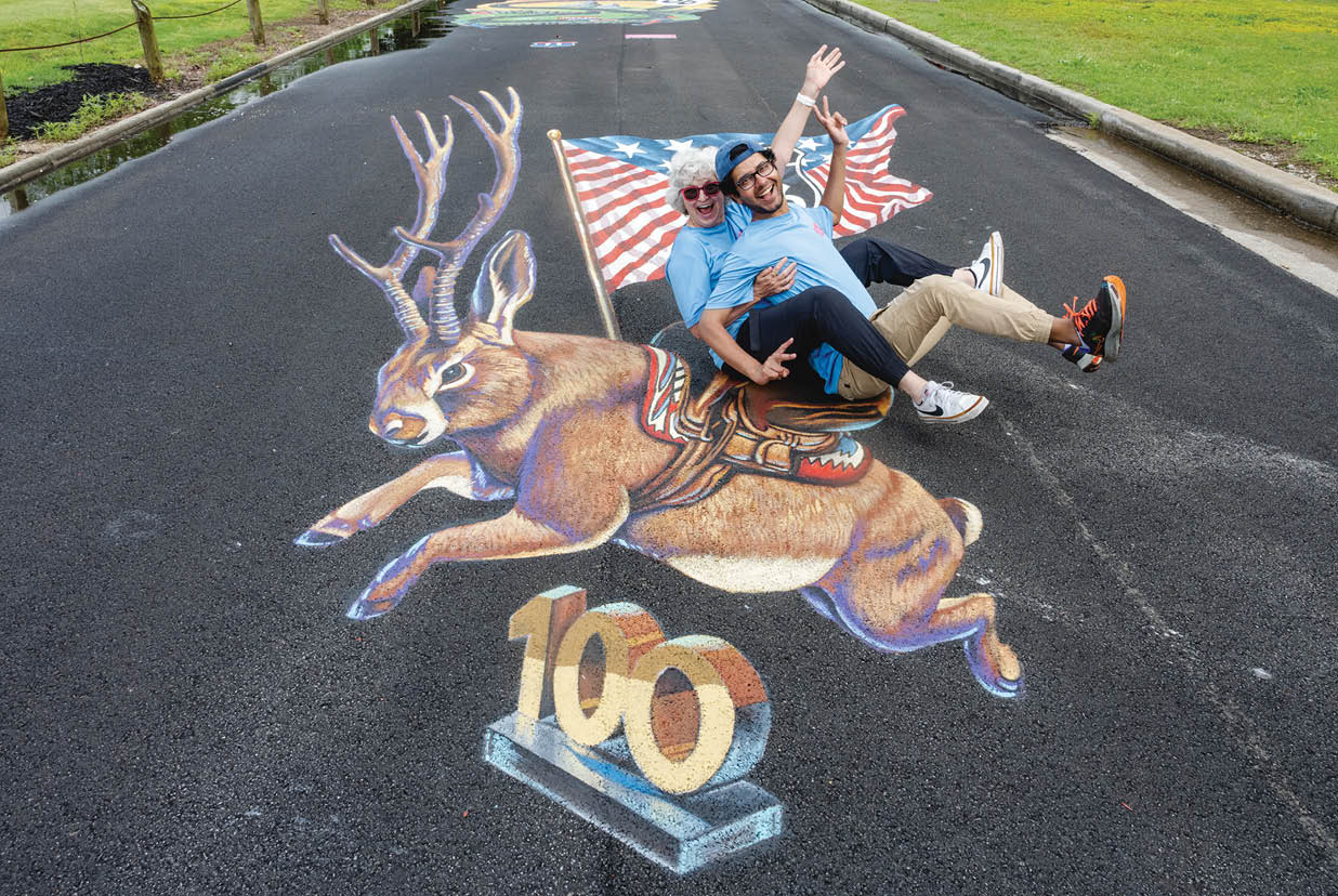 Two men are sitting on a street, one on top of the other, with a deer painted on the road. AI generated content