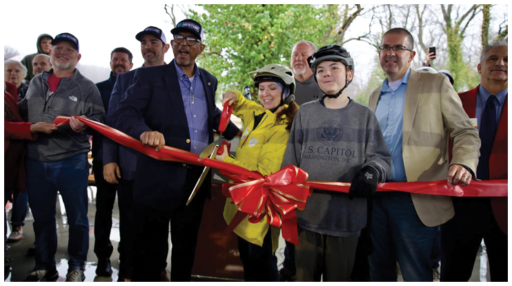 A group of people are gathered for a ribbon cutting ceremony. A man in a yellow jacket is holding a pair of scissors, ready to cut the ribbon. There are several other people in the scene, some of whom are wearing ties. The event appears to be an official opening or celebration. AI generated content