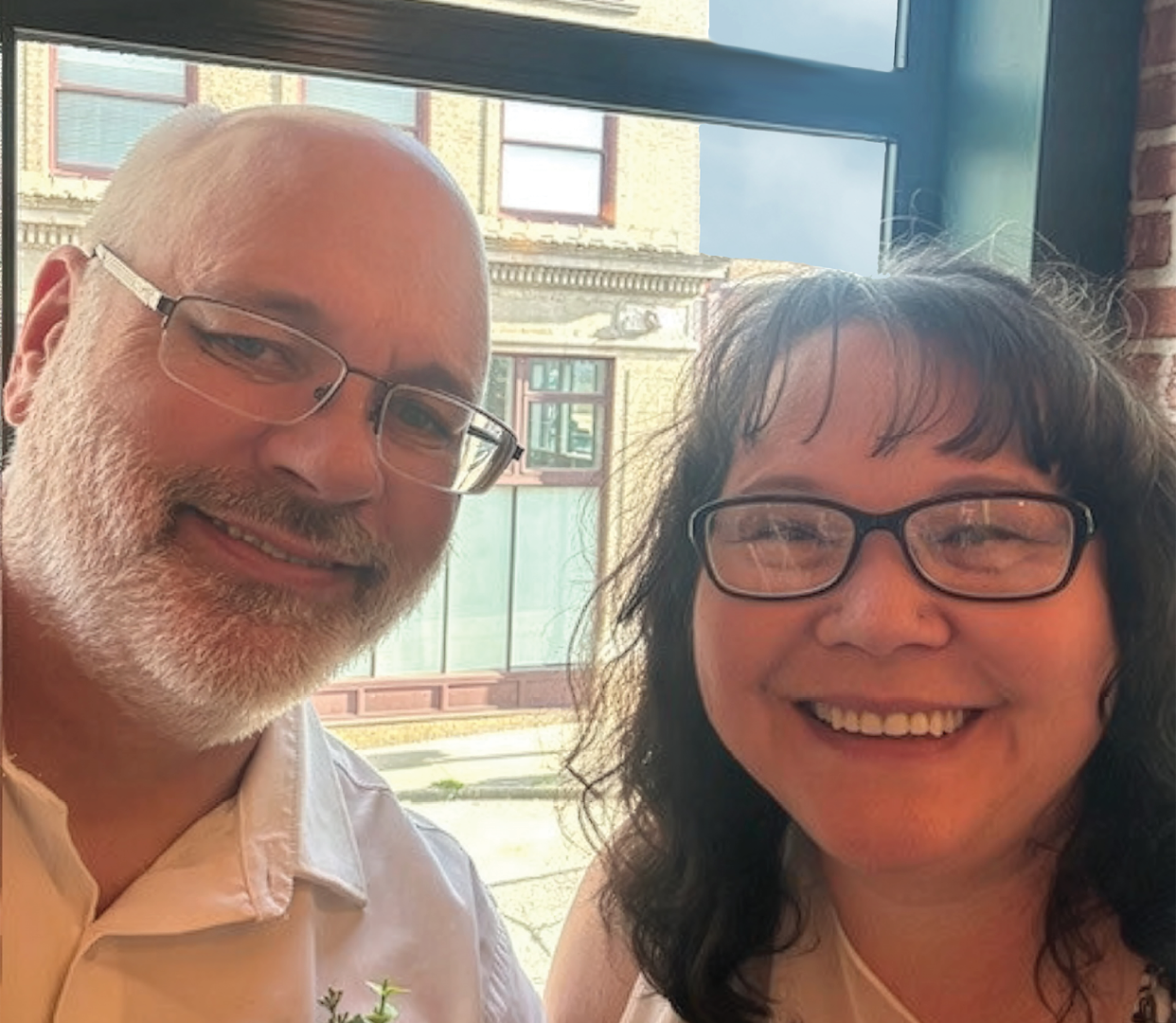 A man and woman are sitting together, both wearing glasses. The woman is smiling and the man is wearing a white shirt. AI generated content