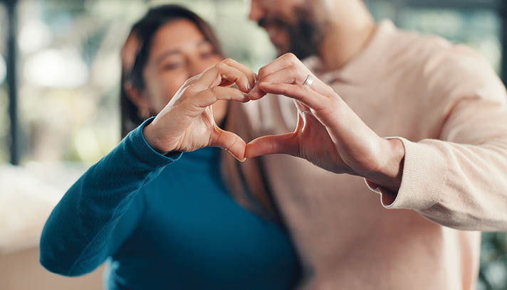 A man and woman are standing close to each other, holding their hands in the shape of a heart. AI generated content