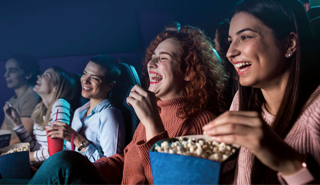 Group of cheerful people laughing while watching movie in cinema.