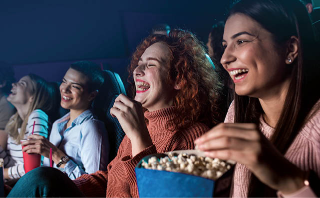 Group of cheerful people laughing while watching movie in cinema.