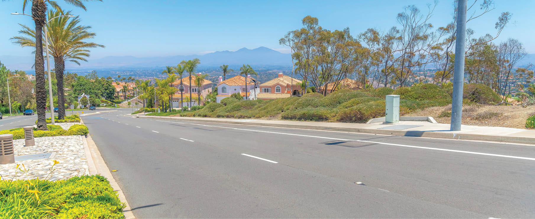 Downhill road near the residential area at Laguna Niguel in California. There are two lanes road on the right near the midian barrier with lamp posts, bushes and palm trees.