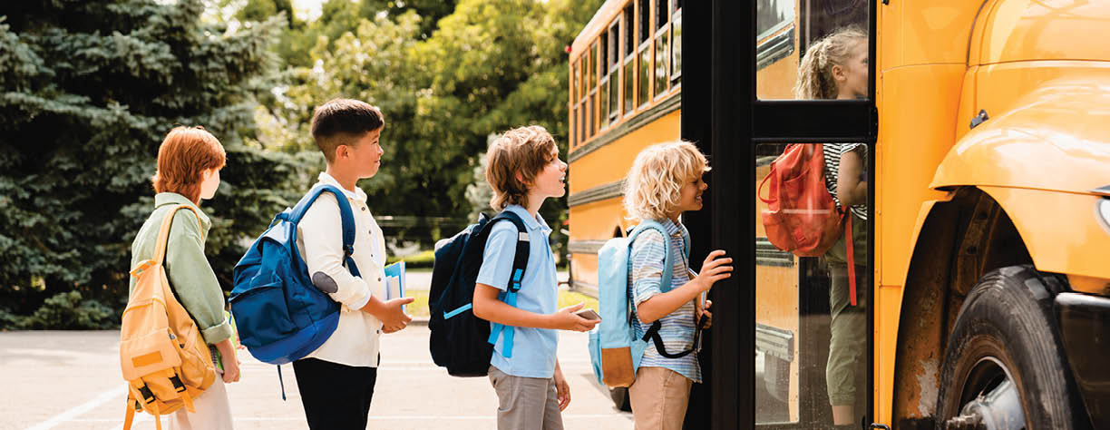 Multiethnic mixed-race pupils classmates schoolchildren students standing in line waiting for boarding school bus before starting new educational semester year after summer holidays