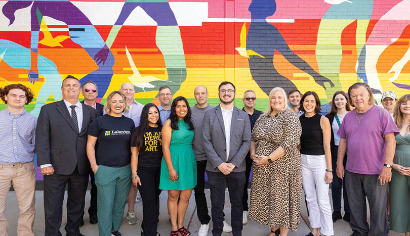A group of people standing in front of a colorful wall. Description generated by AI