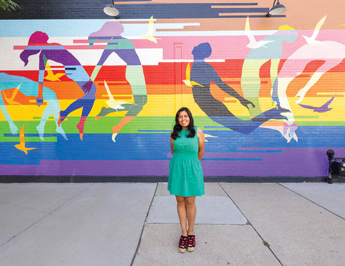 A woman is standing in front of a colorful mural. Description generated by AI