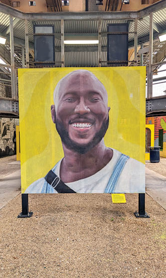 A large yellow and blue painting of a man smiling. Description generated by AI