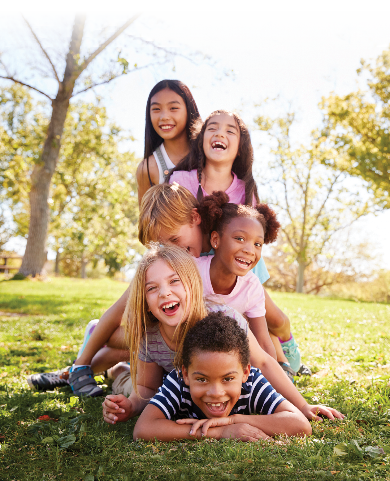 Multi-ethnic group of children lying in a pile in a park