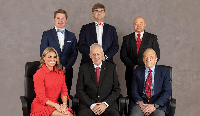 A group of six people, including a man and a woman, are posing for a picture. They are all dressed in suits and ties, with the man on the far left wearing a bow tie. The group is sitting on chairs, with the woman on the left and the man on the right. The other four people are positioned between them, creating a well-organized and professional appearance. AI generated content