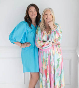 Two women standing next to each other, one wearing a blue dress and the other wearing a pink and white dress. Description generated by AI