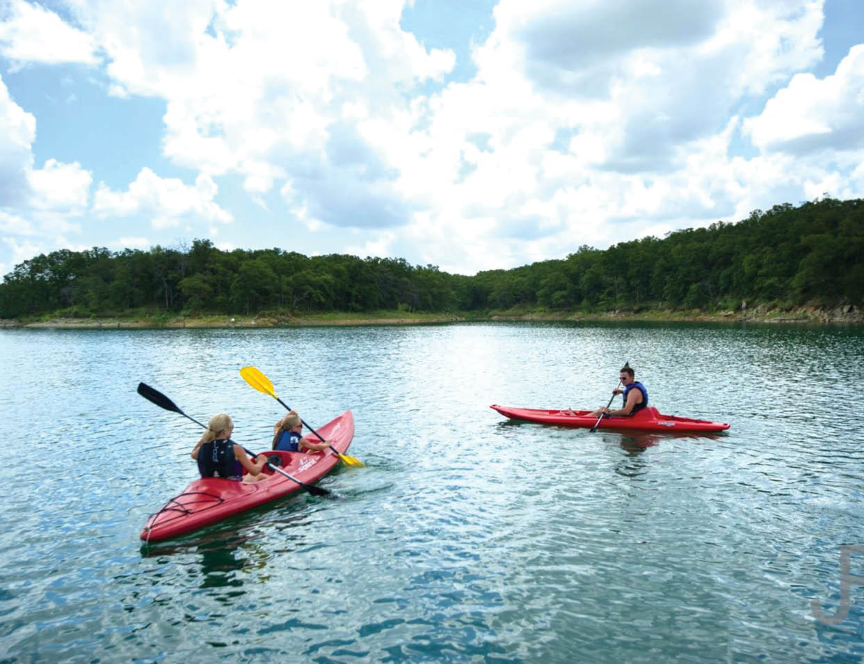 Three people are in red kayaks on a lake. Description generated by AI