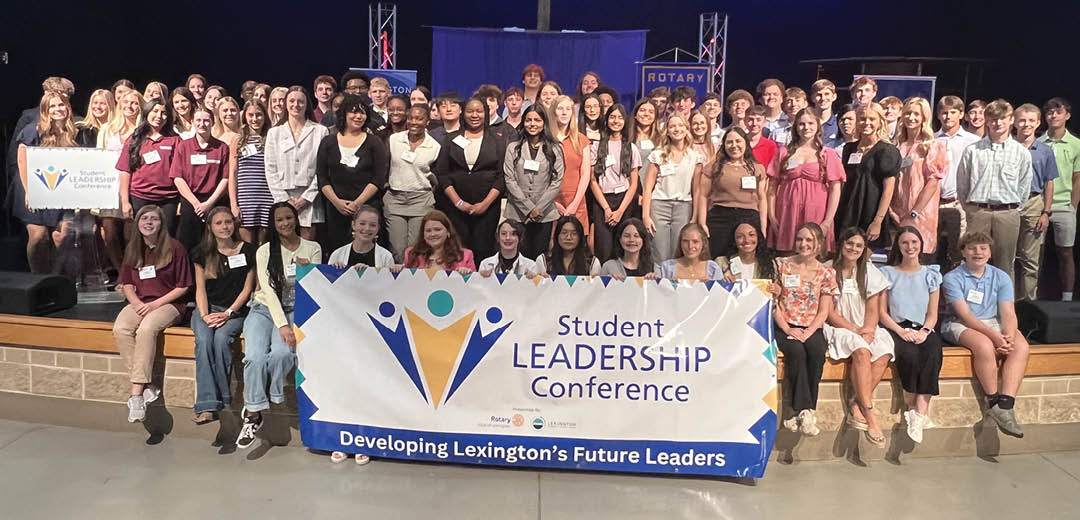 A group of people standing in front of a sign that says “Student Leadership Conference". Description generated by AI