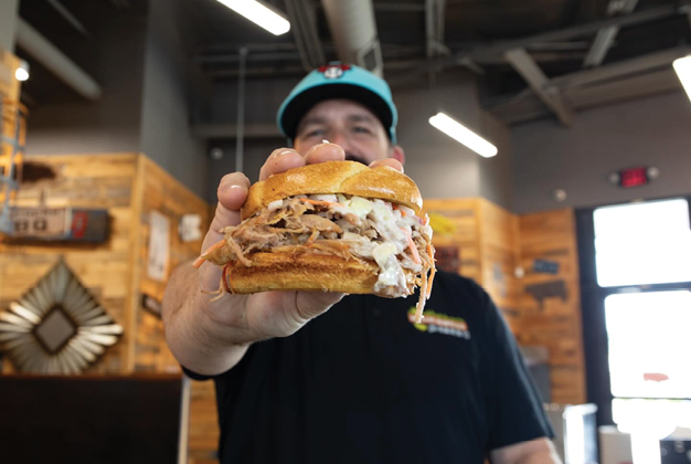 A man holding a large sandwich. Description generated by AI