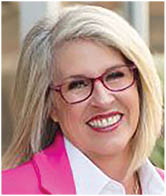 A woman wearing a pink jacket and glasses. Description generated by AI