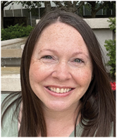A woman with red hair and freckles smiling at the camera. Description generated by AI