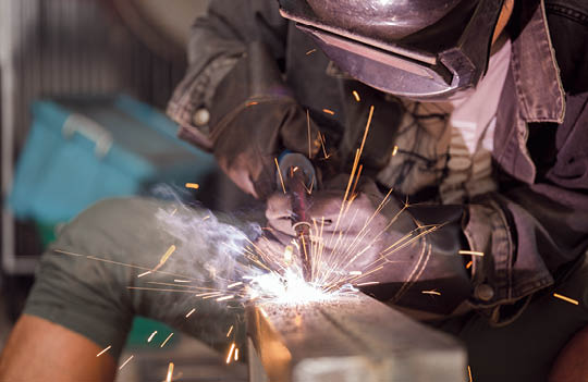 Male worker welding steel, sparks from light, protective masks and gloves increase safety.