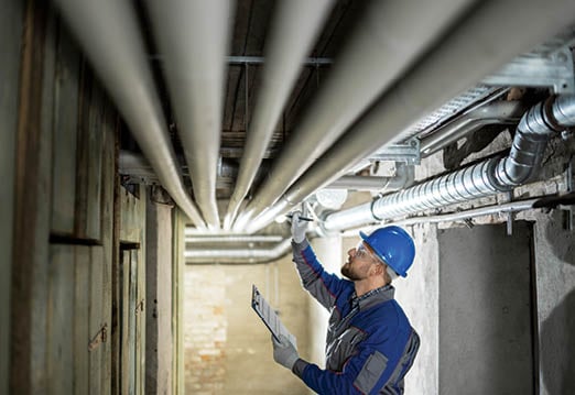 Male Worker Inspecting Water Pipes For Leaks In Basement