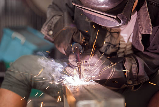 Male worker welding steel, sparks from light, protective masks and gloves increase safety.