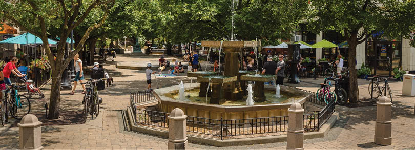 A fountain in a park with people around it. Description generated by AI