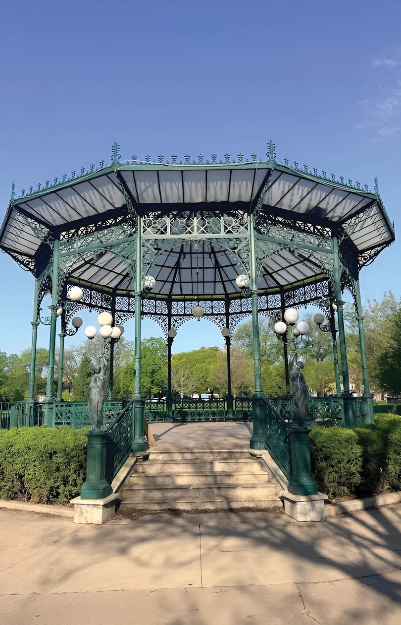 A green gazebo with a white roof and a fence around it. Description generated by AI