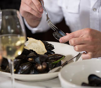 A man is eating mussels from a bowl. Description generated by AI