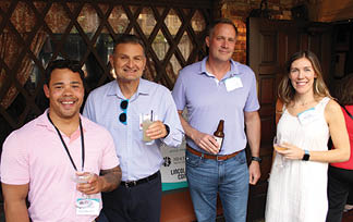 Four people are standing together, holding drinks in their hands. Description generated by AI