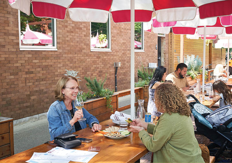 A group of people sitting at a table under a red and white umbrella. Description generated by AI
