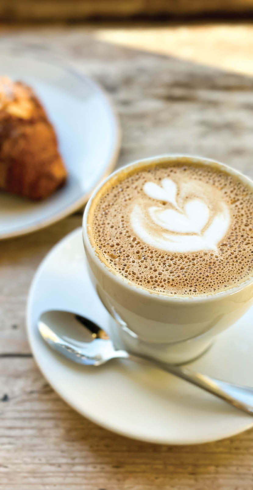 French style breakfast in a cafe. Latte art coffee with freshly baked croissant on a wooden table. pot