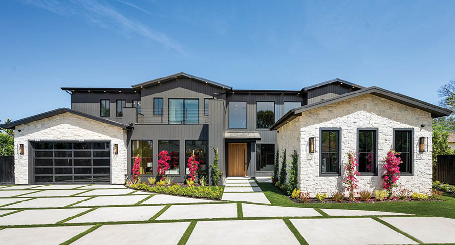 Modern luxury house with a spacious driveway and landscaped garden under a clear blue sky.