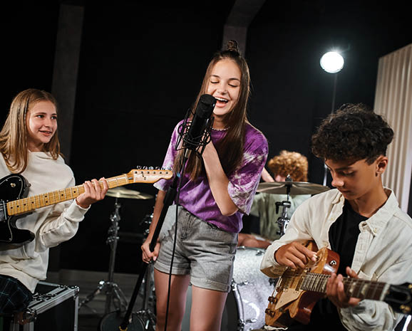 A lively group of teens passionately plays instruments and sings in a cozy music studio.