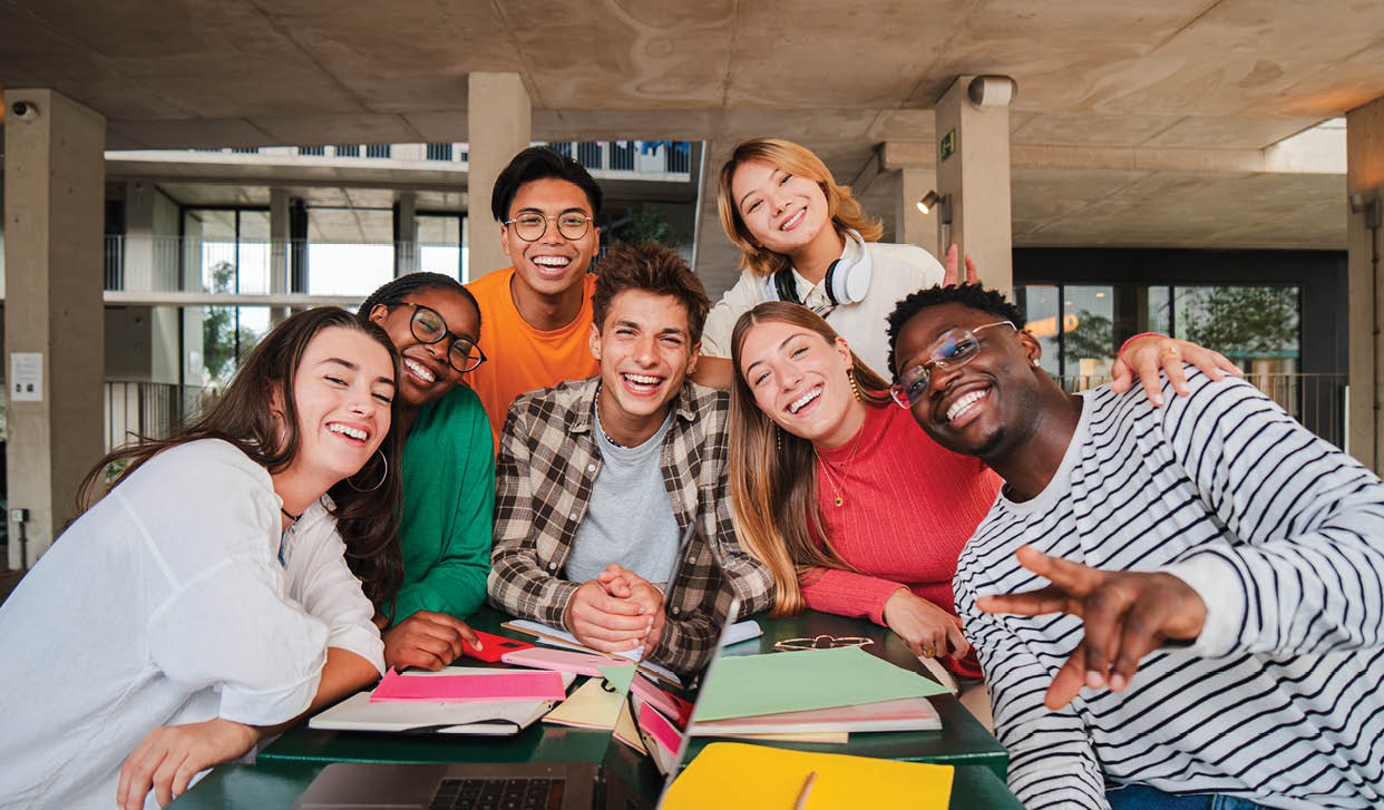 Happy young university students smiling and looking at camera enjoying together sitting in the library or classroom. Multiracial teenage friends laughing on a study break at campus. High school people. High quality photo