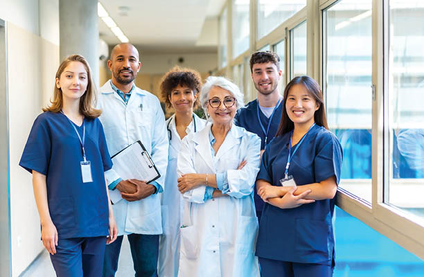 Portrait featuring a multi-ethnic medical team smiling confidently at the camera while gathered in a bustling hospital corridor