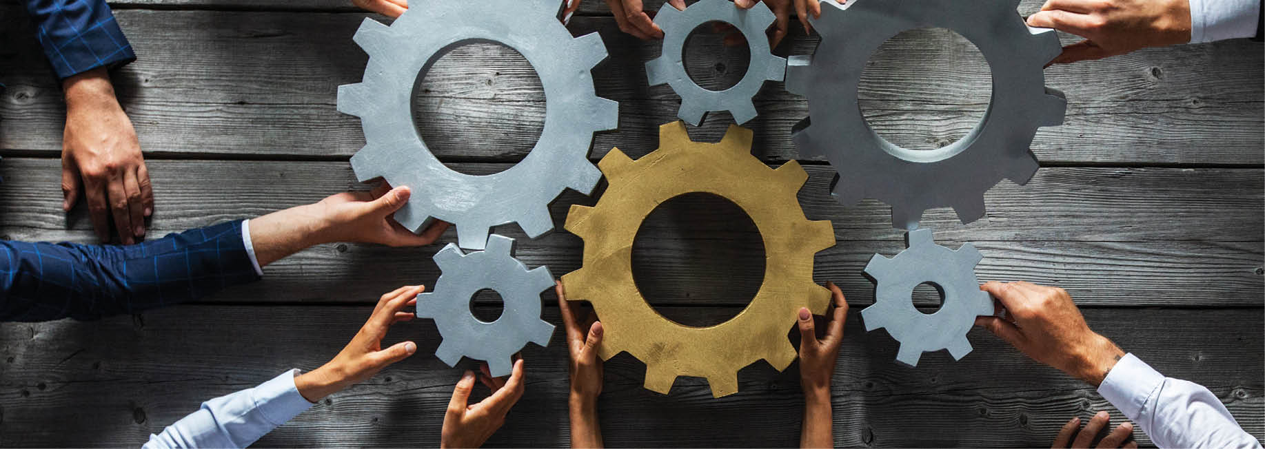 Group of business people joining together silver and golden colored gears on table at workplace top view