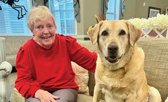 An elderly woman is sitting on a couch next to a large brown dog. AI generated content