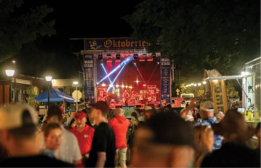 A large crowd of people are gathered in a field, watching a concert. The performers are on a stage with lights illuminating them. The audience is standing close to the stage, enjoying the show. AI generated content