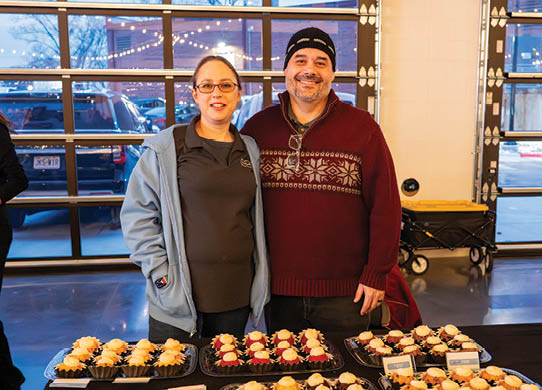 A man and woman are standing in front of a table full of cupcakes. AI generated content