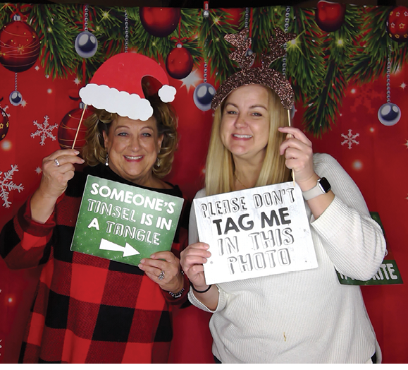 Two women wearing Santa hats and holding signs that say “someone please tag me in this photo." AI generated content