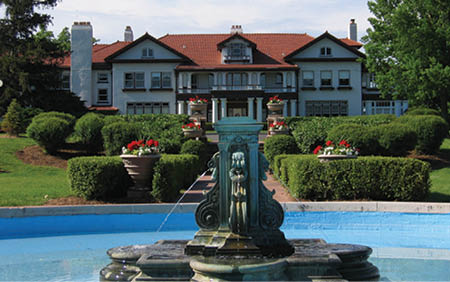 A large fountain with a statue of a woman is located in front of a large white house. AI generated content