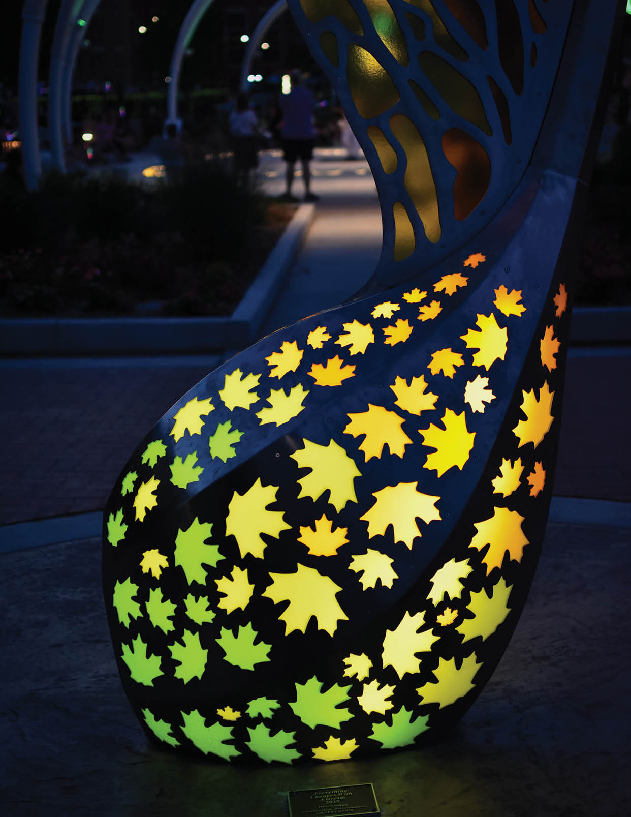 A sculpture of a tree with leaves is lit up at night. AI generated content