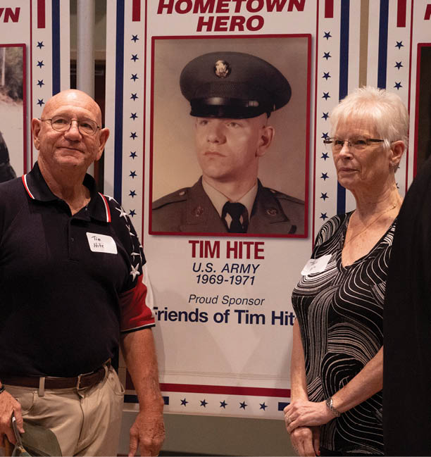 A man and woman stand in front of a display of photos, including one of a man in a military uniform. AI generated content