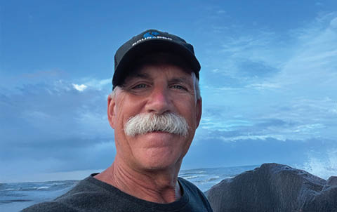 A man with a mustache and hat is standing on a beach. AI generated content