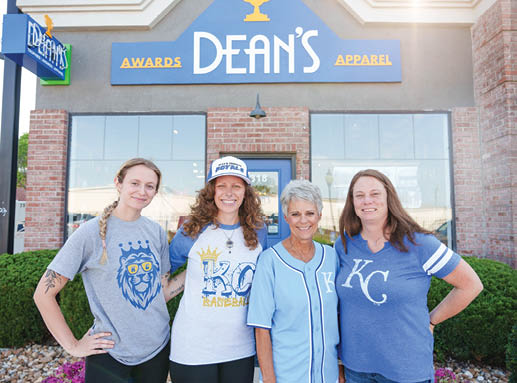 Four women pose in front of a store, wearing blue shirts and hats. AI generated content