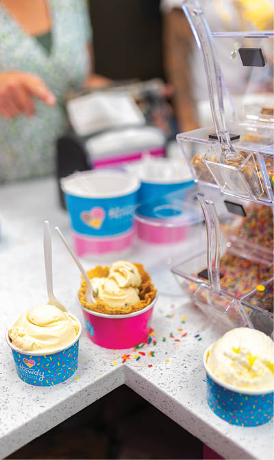 A woman is scooping ice cream into a pink bowl. There are three bowls of ice cream on the counter, one of which is pink. AI generated content
